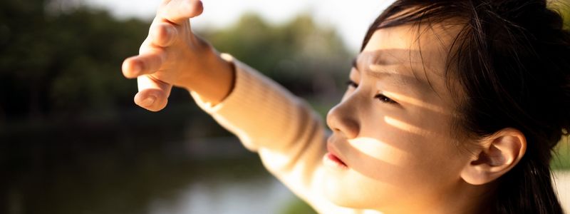 Young woman shielding her face from the sun with her hand, illustrating the importance of sun protection and daily suncare routines.