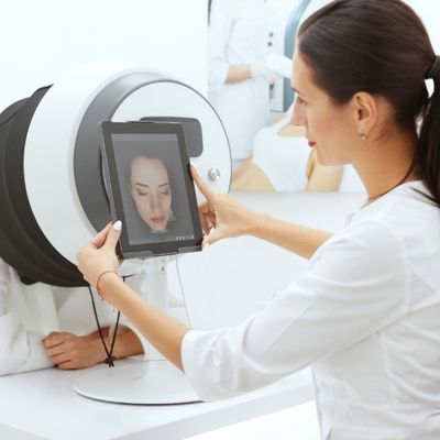 Two women interacting with AI beauty technology; one is using an AI-powered device to perform skin analysis on the other, demonstrating the role of AI in personalised skincare.